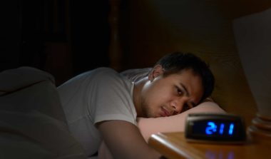 Depressed man suffering from insomnia lying in bed